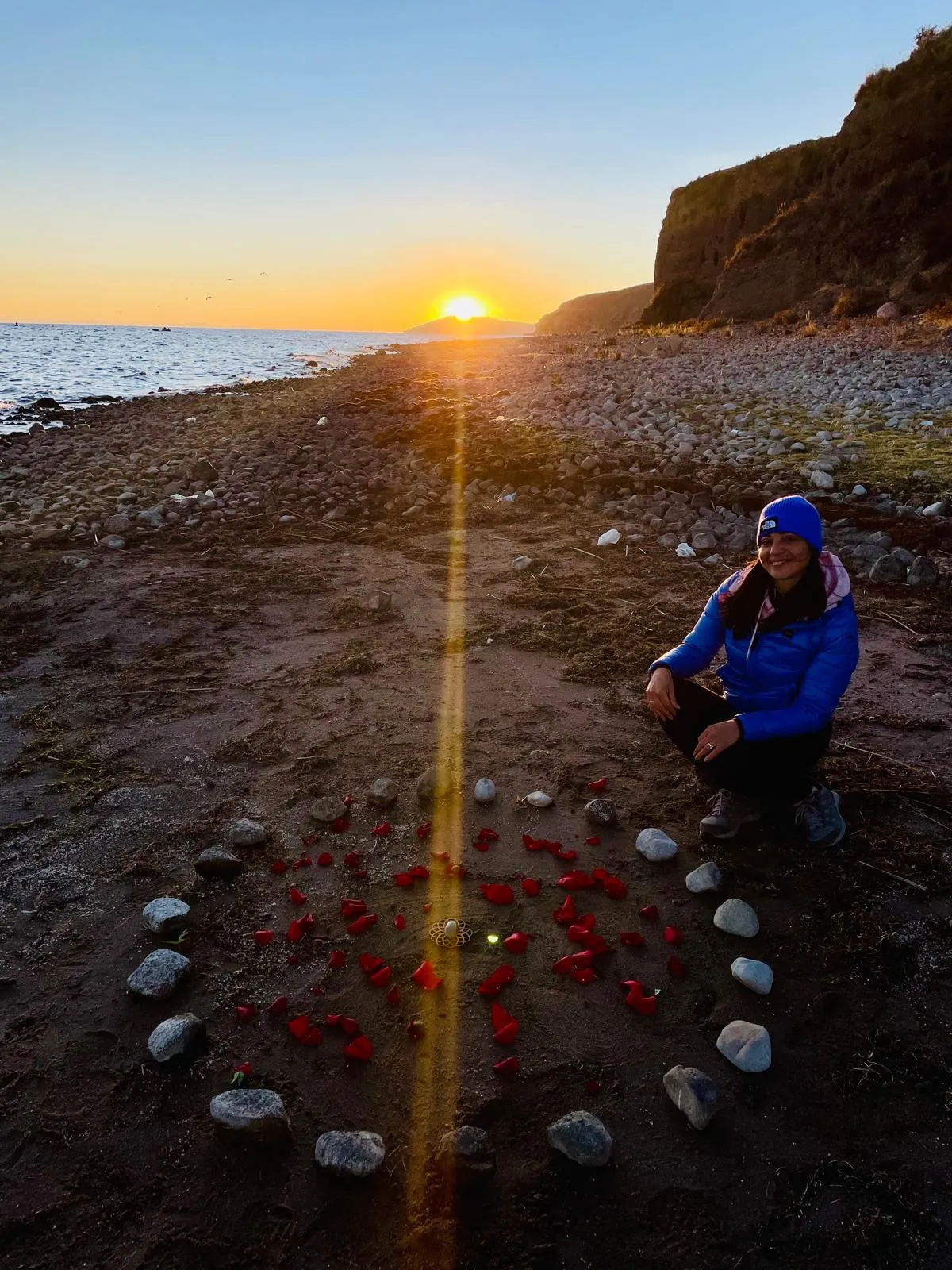 Teresa Ferrantino accovacciata su una spiaggia al tramonto, accanto a un cerchio di pietre e petali